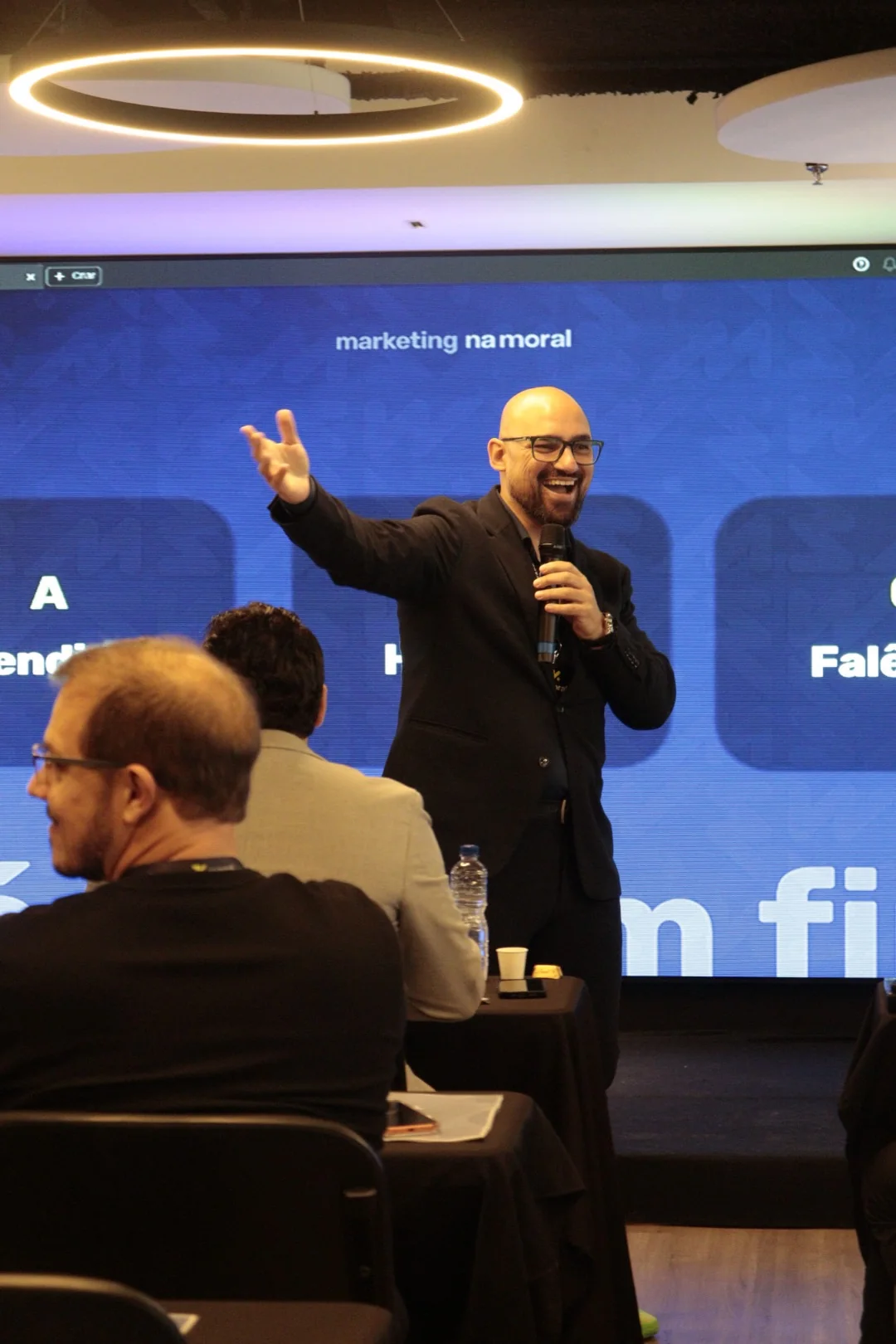 Djeison Moreira no palco do Na Moral Experience enquanto participantes acompanham